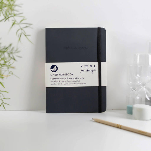 Minimalist charcoal A5 notebook with recycled leather cover and elastic closure, shown on white desk with wooden pencil and plants, perfect for sustainable home office setup