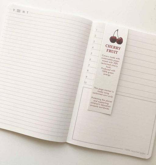 Interior view of an open notebook showing lined pages and a cherry fruit branded bookmark with numbered sections. The page displays recycled paper certification and sustainability information.