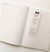 Interior view of an open notebook showing lined pages and a cherry fruit branded bookmark with numbered sections. The page displays recycled paper certification and sustainability information.