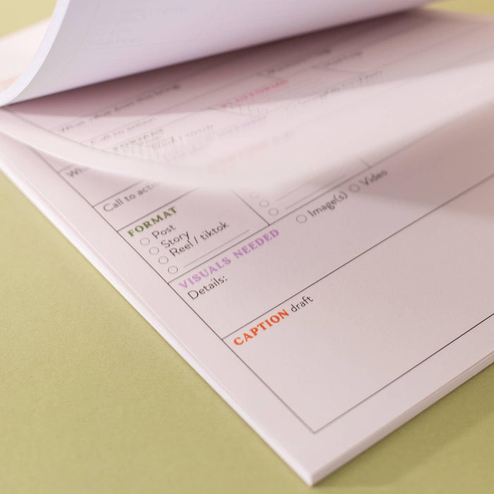 Angled close-up showing multiple tear-away pages of the content planner, highlighting the format checkboxes and caption section. Pink and orange text headers visible on white recycled paper, demonstrating the pad's depth and page separation against a sage green background.