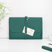 Emerald green recycled leather document wallet with ETHOS branding lying flat on white surface. Features a white product tag and string closure system. Bamboo leaves visible in background corner.