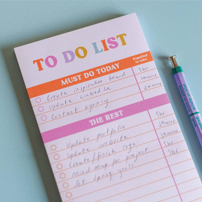 A filled To Do List pad showing business tasks like "Update LinkedIn" and "Contact agency" in the "Must Do Today" section, with longer-term tasks listed under "The Rest". The pad features orange and pink section headers with estimated time allocations next to each task.