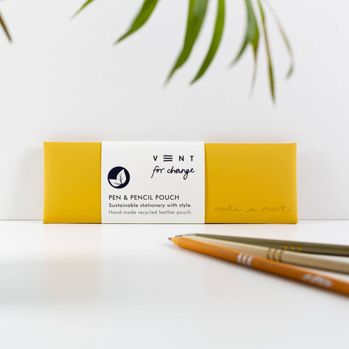 Yellow recycled leather pen pouch by Vent lying flat on white surface with bamboo pencils beside it. Product band shows Vent for Change logo and sustainable stationery messaging.