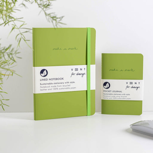 Two green VENT notebooks displayed together against a white background - a larger lined notebook and smaller A6 pocket journal. Both feature "make a mark" text and branded paper bands. Green foliage visible in the corner and a grey pencil at the bottom of the frame.