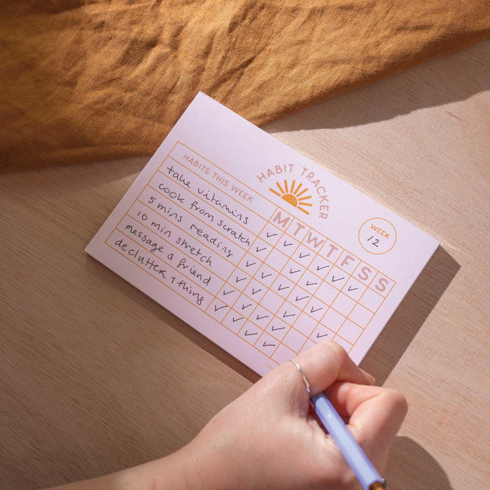 Entrepreneur using Weekly Habit Tracker pad to track business development habits including daily reading and networking, shown with gold foil details and handwritten entries