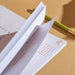 Close up of weekly planner pad's thick paper stack and binding, showing colourful habit tracking dots and clean tear-off edge. Green pencil for scale demonstrates premium paper quality.