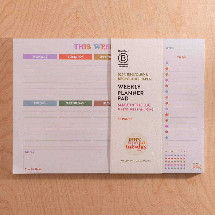 Weekly planner pad showing product details and B Corp certification. Features 52 recyclable pages, plastic-free packaging claim, and 'Made in the U.K.' statement. Displays full weekly layout with colourful day tabs and habit tracker.