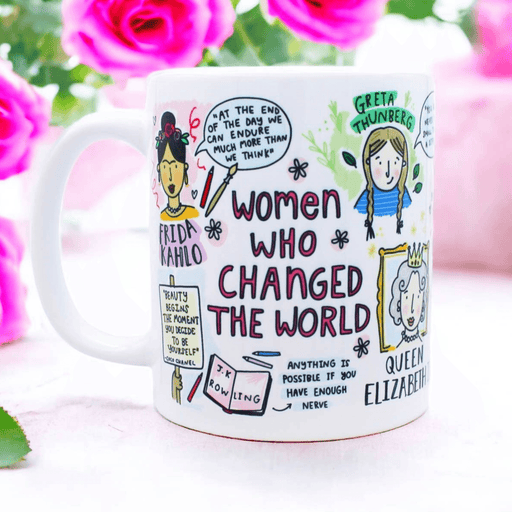 White ceramic mug featuring whimsical illustrated portraits and quotes from influential women including an artistic representation of historical figures, with pink roses in the background. The mug displays hand-drawn text reading 'Women Who Changed the World' along with inspirational quotes and decorative elements in a playful sketch style.